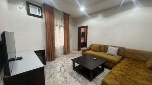 Una sala de estar con un sofá, una mesa de centro, un televisor y una ventana con cortinas.