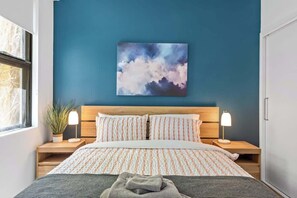 Ein Schlafzimmer mit einem Bett, zwei Nachttischen, einem Wandbild und einem Fenster.