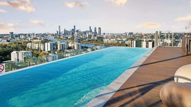 Ein Infinity-Pool auf dem Dach mit Blick auf die Stadt, einer Holzterrasse und einem Verbotsschild für Schwimmer.