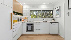Een moderne keuken met witte kasten, een inbouwoven, een vaatwasser en een raam met uitzicht op bomen.