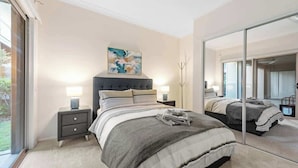 A bedroom with a bed, bedside tables, a mirror, and a painting on the wall.