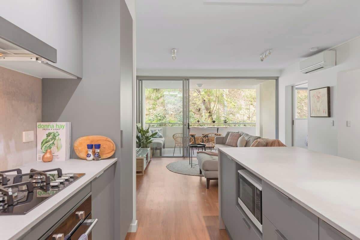 A modern kitchen with a gas stove, a dining area with a round table and chairs, and a view of the outdoors through large windows.