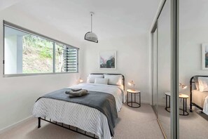 Ein modernes Schlafzimmer mit Bett, Nachttischen, einer Pendelleuchte und einem großen Fenster.