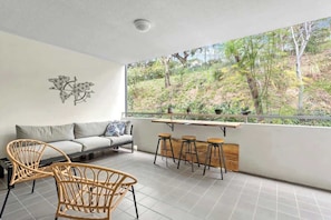 Ein Balkon mit einer Couch, Stühlen und einer Bar mit Hockern.