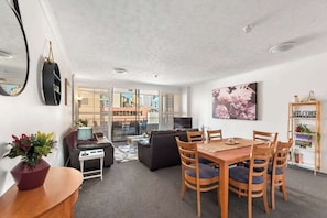 A modern living room with a dining area, a sofa, a TV, and a large window. - Amazing Astor ~ 2bed, 2bath, 1car, Pool! (Brisbane)