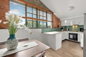 A kitchen with a brick wall, a window with blinds, white cabinets, a countertop, and a sink. - Historic Warehouse in New Farm (Brisbane)