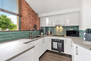 A modern kitchen with white cabinets, a brick wall, and a green-tiled backsplash. - Historic Warehouse in New Farm (Brisbane)