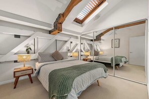 A bedroom with a sloped ceiling, a skylight, a bed with a green blanket, bedside tables with lamps, and a large mirror. - Historic Warehouse in New Farm (Brisbane)