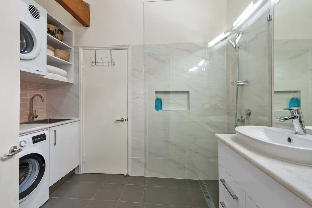 A bathroom with a washing machine, a sink, and a glass shower enclosure.