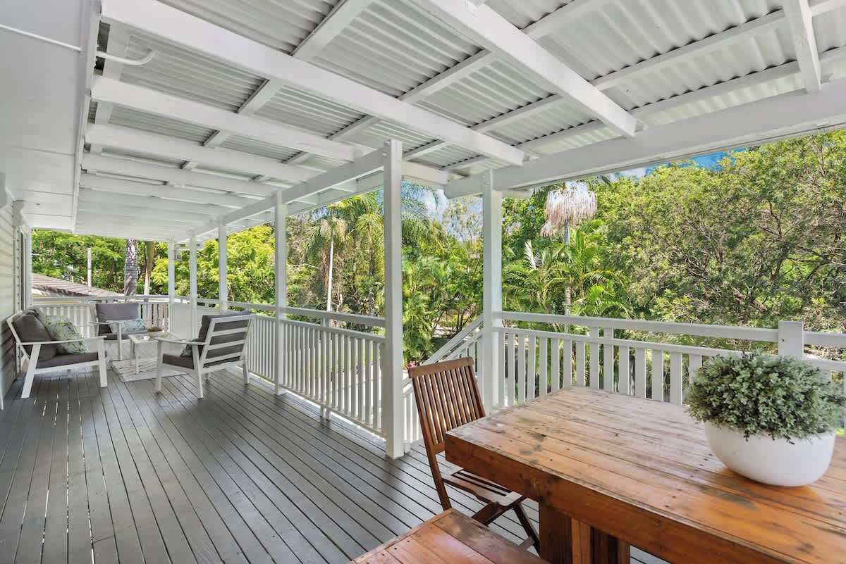 A covered outdoor area with a wooden deck, white railings, and a table with chairs.