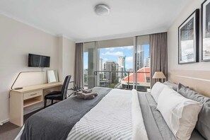 Habitación de hotel con cama, escritorio, silla, televisor y vistas a la ciudad.
