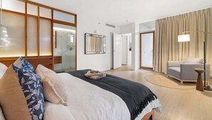 Quarto de hotel com uma cama grande, uma mesinha de cabeceira, uma cadeira, um espelho e um abajur.
