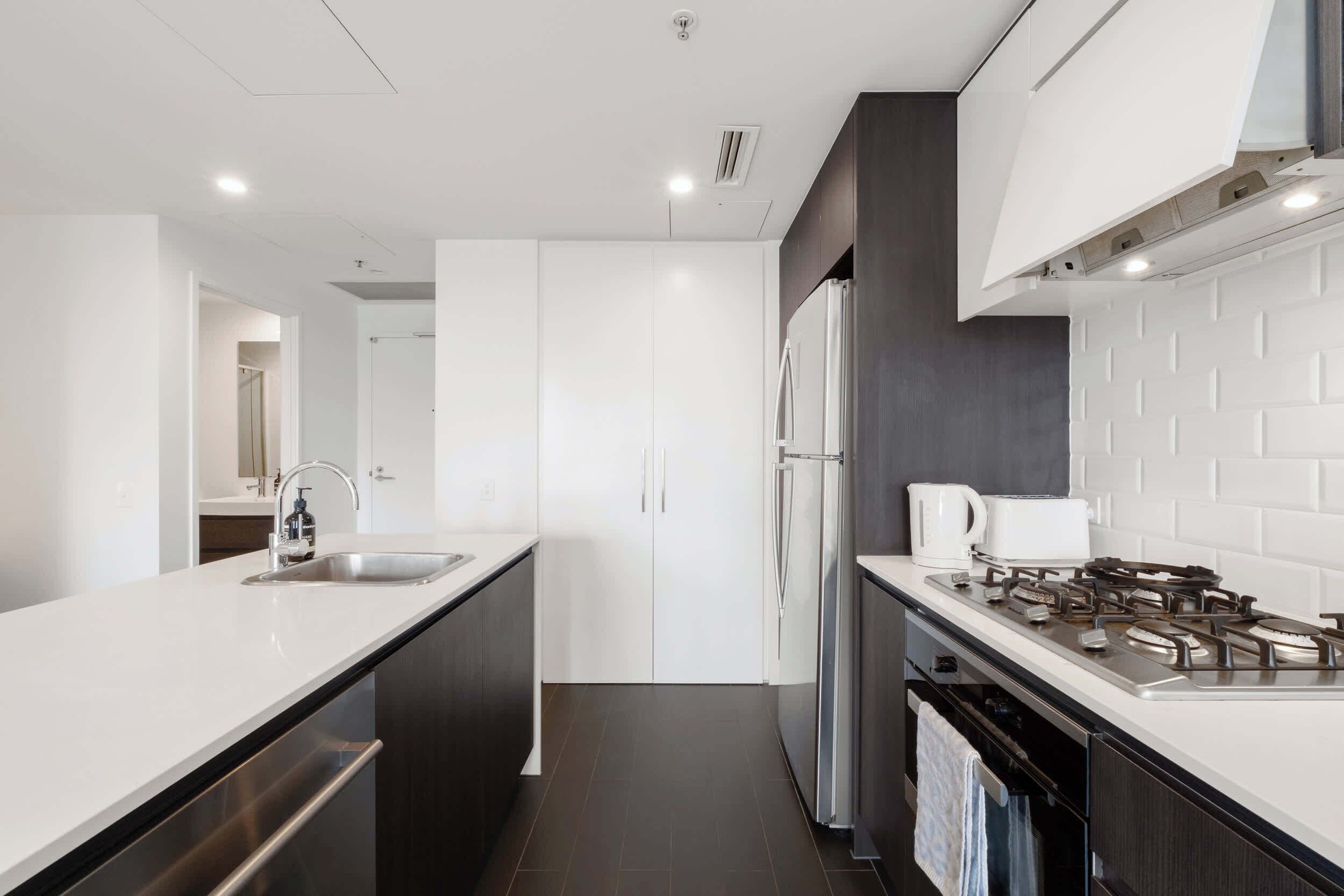 A modern kitchen with white cabinetry, a stainless steel sink, a built-in stove, and a refrigerator.