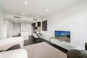 A modern living room with a flat-screen TV, a dining area, and a kitchen in the background. - Fab! Skyline CBD Views Over South Bank! (Brisbane)