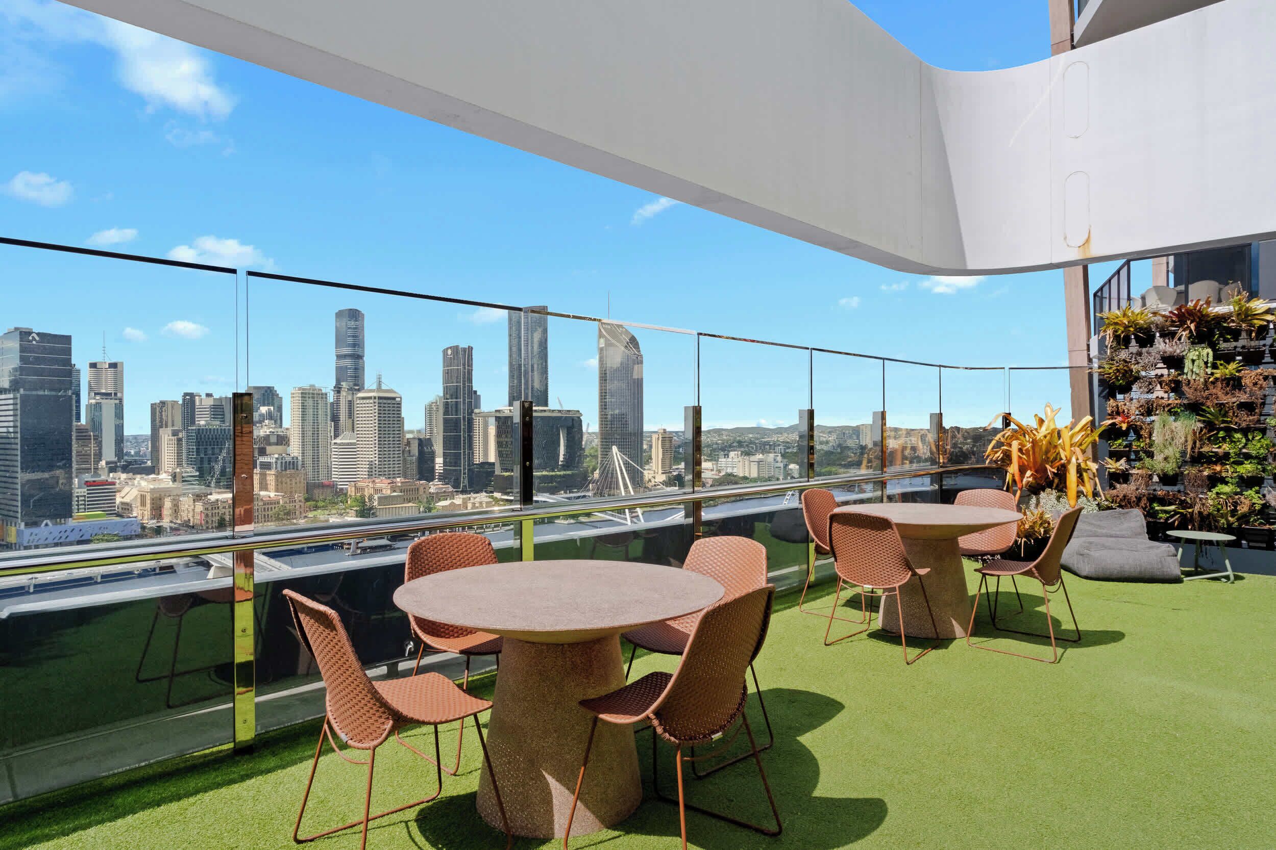A rooftop terrace with a city skyline view, round tables, and chairs, and a vertical garden.