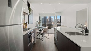 A modern kitchen with a central island, a dining area with chairs, a large window with a city view, and a built-in sink.