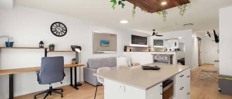 A modern kitchen with a central island, wooden ceiling, and hanging plants.