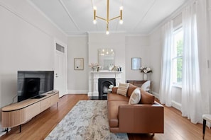 A living room with a TV, sofa, fireplace, and a chandelier. - Art Deco With Modern Twist! 1bed-1bath-1car-new Farm (Brisbane)