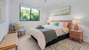 Una camera da letto con un letto, comodini, una sedia, una finestra e una ventola a soffitto.
