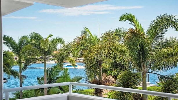 Un balcone con vista su un corpo d'acqua, palme e una costa in lontananza.
