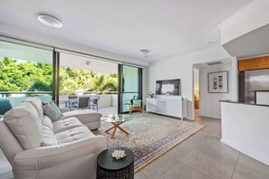 A modern living space with a sofa, coffee table, and a view of greenery through large windows. - New Farm Water Views! 2bed/2bath/1car (Brisbane)
