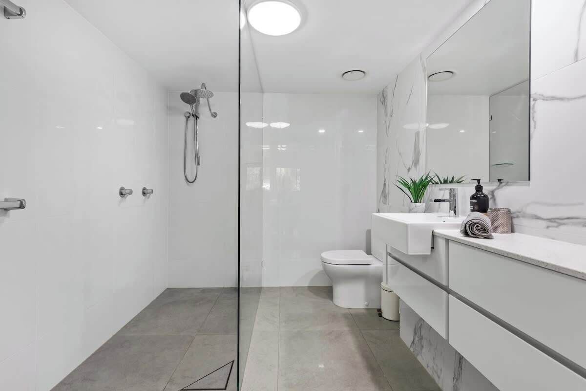 A modern bathroom with a glass shower enclosure, a toilet, and a vanity with a mirror and sink.