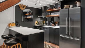 Eine moderne Küche mit Kochinsel, schwarzen Schränken, Edelstahlgeräten und einer Bär-Motiv-Wanddekoration.