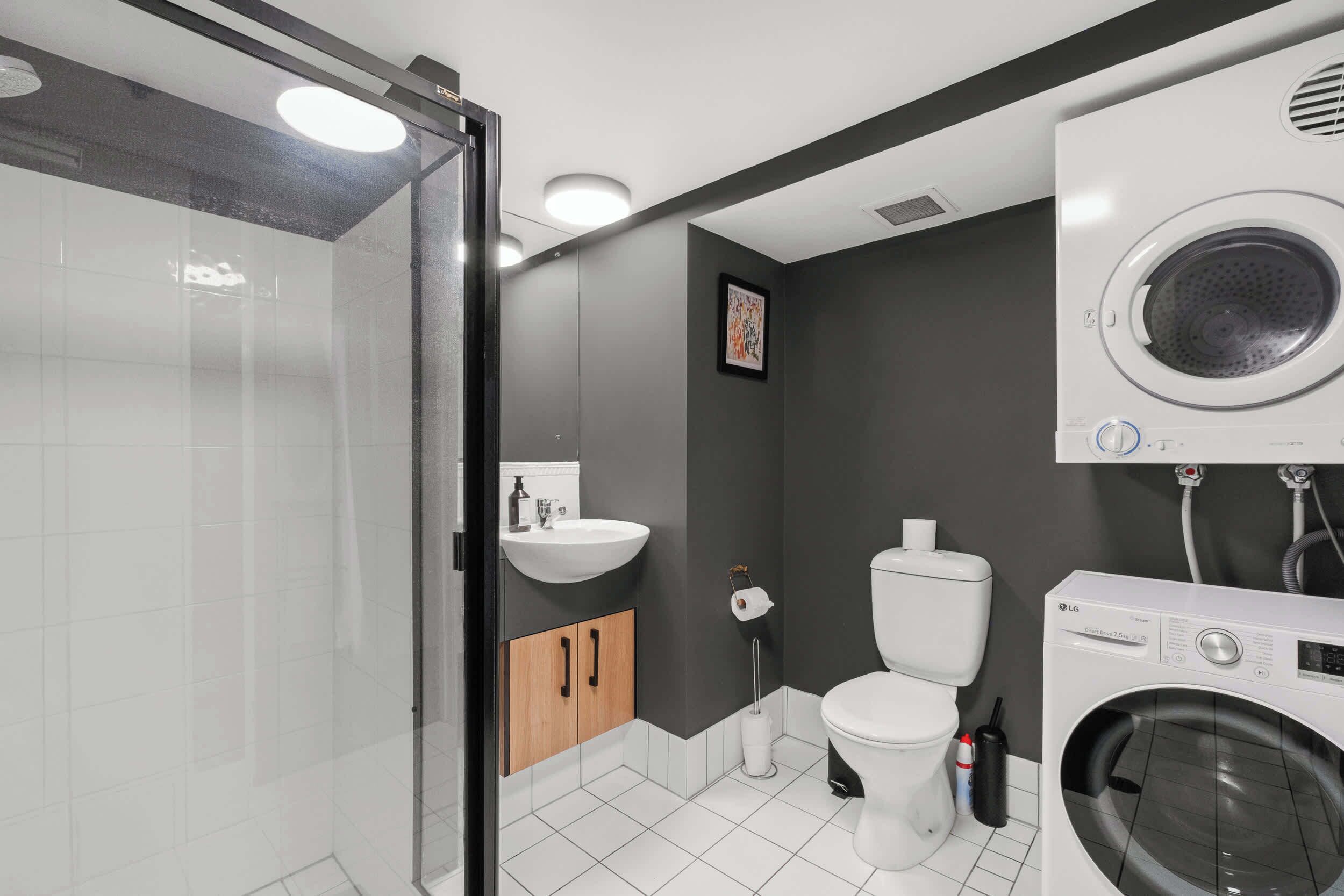 A modern bathroom with a glass shower enclosure, a sink, toilet, and a built-in washing machine.
