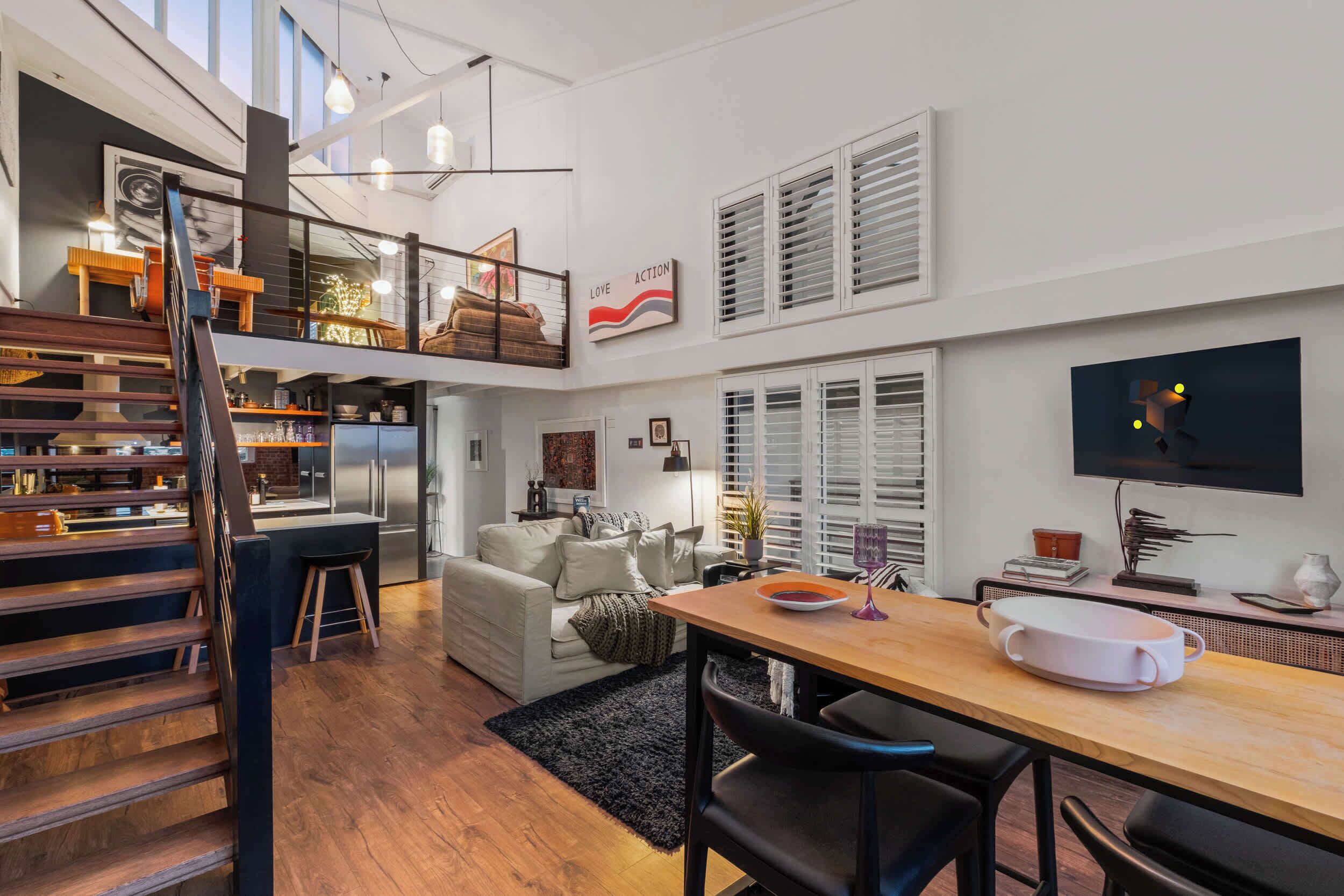 A modern interior with a staircase, dining area, kitchen, and a flat-screen TV.