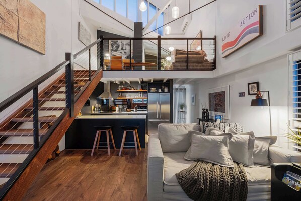 Ein modernes Interieur mit Treppe, Küchenbereich, Wohnzimmer mit Sofa und Kunstwerken an den Wänden.