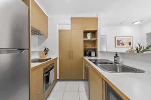 A modern kitchen with stainless steel appliances, wooden cabinets, and a white countertop. - Home Away From Home! 2bed/1bath/car/pool~2kms CBD (Brisbane)