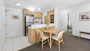 A compact kitchen with a refrigerator, a dining table with chairs, and a bench. - Home Away From Home! 2bed/1bath/car/pool~2kms CBD (Brisbane)