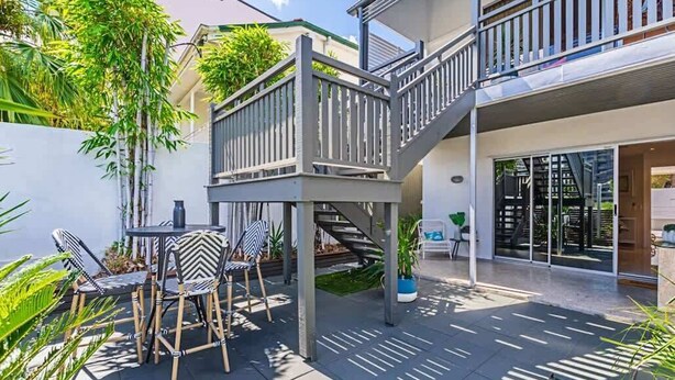 Un patio exterior moderno con una escalera, una mesa de comedor con sillas y plantas en macetas.