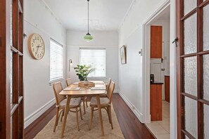 A dining area with a wooden table, chairs, a clock, and a hanging light fixture. - Art Deco in Ascot! ~ 2 Bed / 1 Bath / 1 Car (Brisbane)