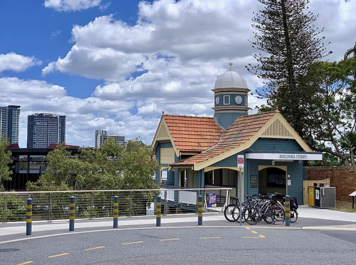 A building with a dome and clock tower, labeled 'BULIMBA FERRY,' with bicycles parked outside.