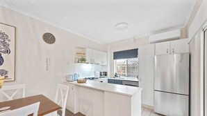 Eine moderne Küche mit weißen Schränken, einem Edelstahlkühlschrank und einem Essbereich mit Holztisch und weißen Stühlen.