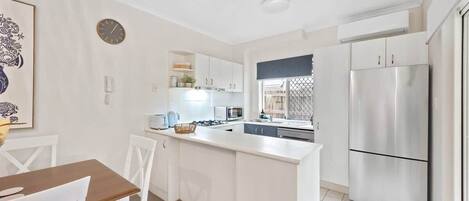 A modern kitchen with white cabinetry, a stainless steel refrigerator, and a dining area with a wooden table and white chairs.