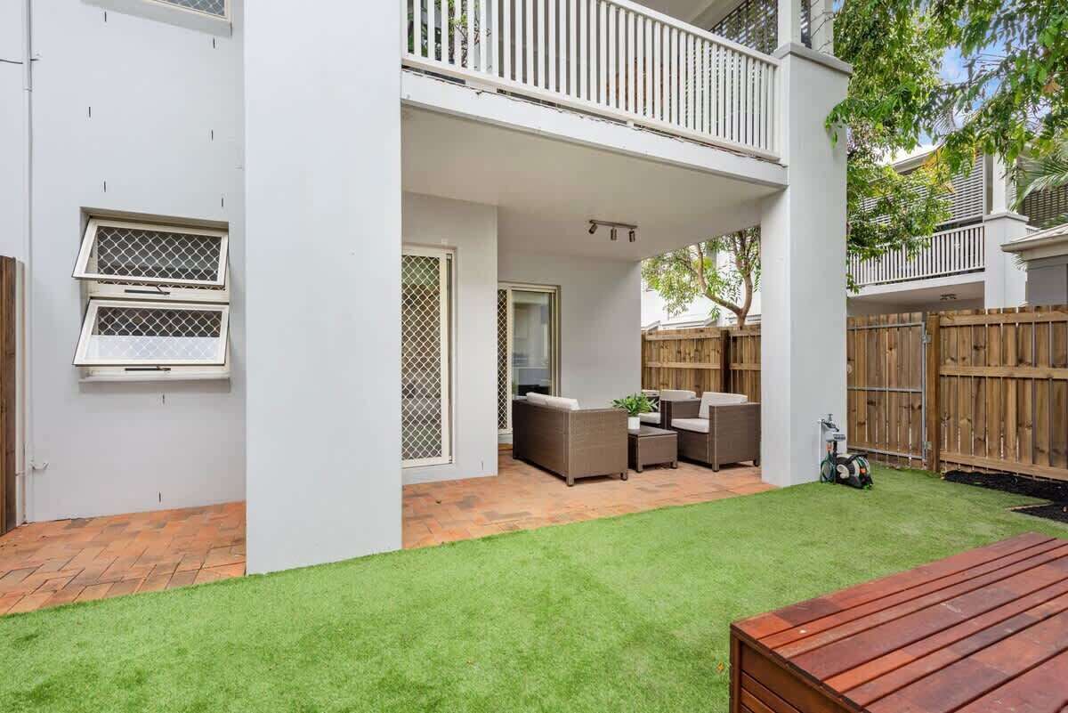 A covered patio area with outdoor furniture, a wooden fence, and a grassy lawn.