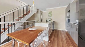 A modern kitchen with a wooden dining table, white chairs, a hanging light fixture, and a staircase. - Convenient + Spacious! 3bed/2.5bath/1car~townhouse (Brisbane)