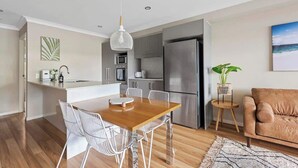 A modern kitchen with a central island, stainless steel appliances, and a dining area with a wooden table and white chairs. - Convenient + Spacious! 3bed/2.5bath/1car~townhouse (Brisbane)