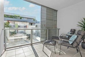 Ein Balkon mit Glastrennwand, zwei gepolsterte Stühle, ein kleiner Tisch und ein Blumentopf.