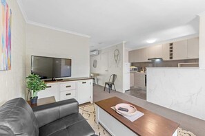 Ein modernes Wohnzimmer mit einem Flachbildfernseher, einem Ledersofa, einem Couchtisch und einer Topfpflanze.