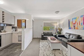 Ein modernes Wohnzimmer mit Sofa, Couchtisch und einer Küchenzeile mit Schränken und einem Fenster.