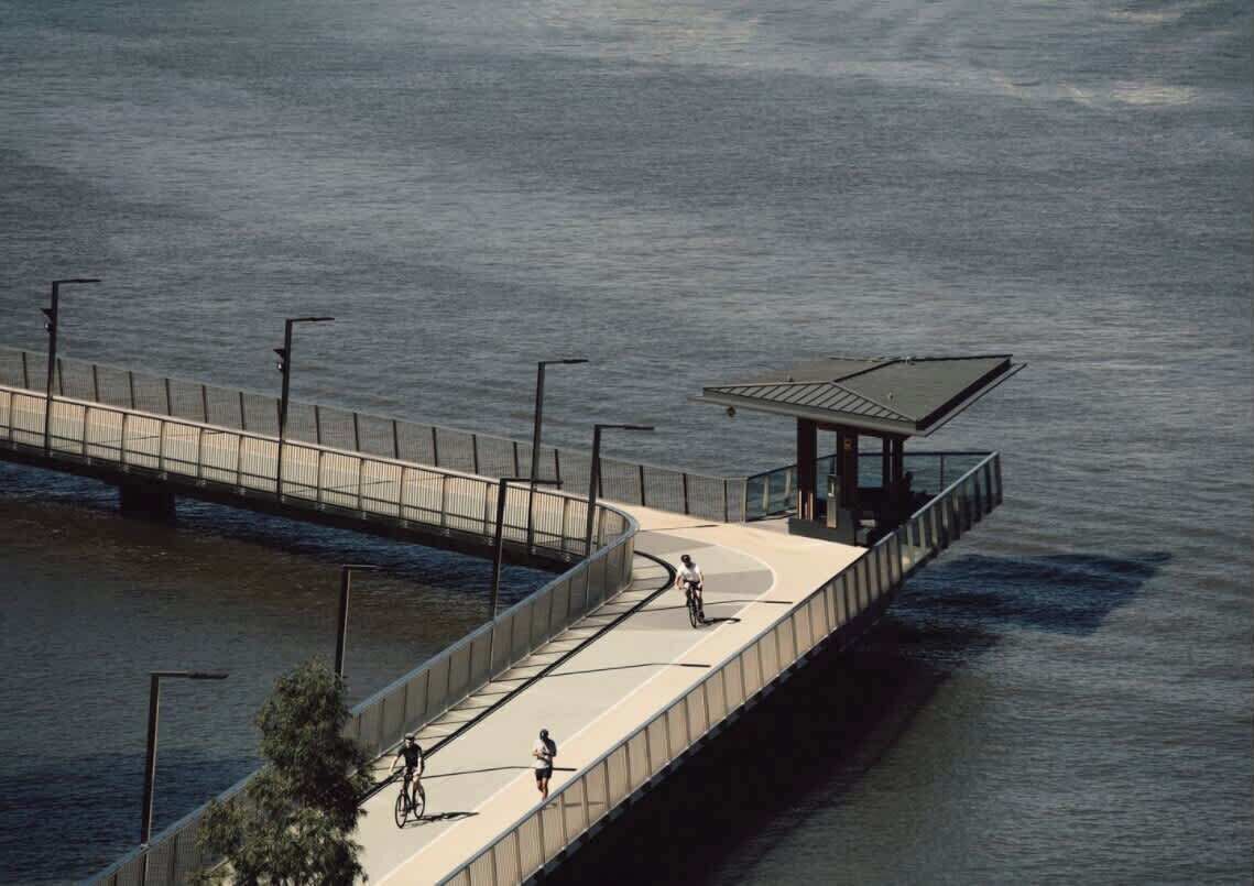 A waterfront pedestrian bridge with a covered seating area and street lamps.