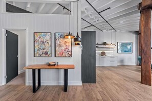 A modern interior with a wooden bench, two abstract paintings, a pendant light, and a kitchen area in the background. - Luxurious Woolstore Living! ~teneriffe (Brisbane)