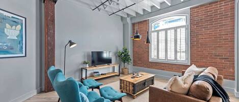 Una sala de estar moderna con televisor, sillones azules, un sofá marrón, una mesa de centro de madera y una pared de ladrillo.