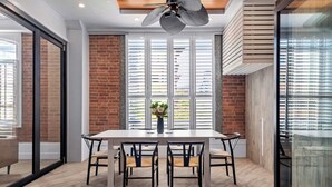 A dining area with a table and chairs, a ceiling fan, and large windows with blinds. - Luxurious Woolstore Living! ~teneriffe (Brisbane)