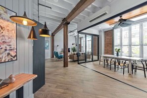 An open-plan office with exposed wooden beams, a long table with chairs, and pendant lighting. - Luxurious Woolstore Living! ~teneriffe (Brisbane)