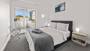 Una habitación de hotel moderna con una cama, una mesita de noche, una lámpara de pared, un ventanal con vistas y una puerta que da a un espacio exterior.