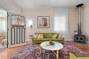 Ein Wohnzimmer mit einem grünen Sofa, einem runden Couchtisch, einem großen Teppich, einem Kamin und einem gerahmten Bild an der Wand.